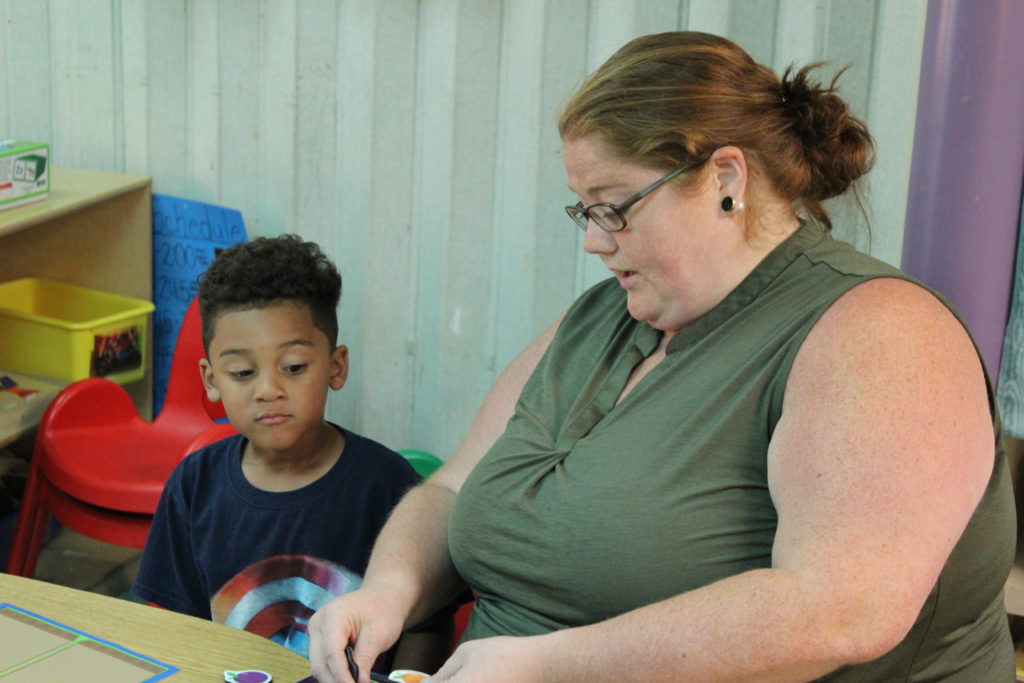 A boy sits with a teacher at a table, with puzzle pieces spread out before them.