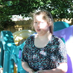 A woman stands in the shade on a playground.