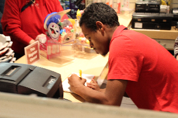 A young man leans over the counter of a store, completing a customer order form.