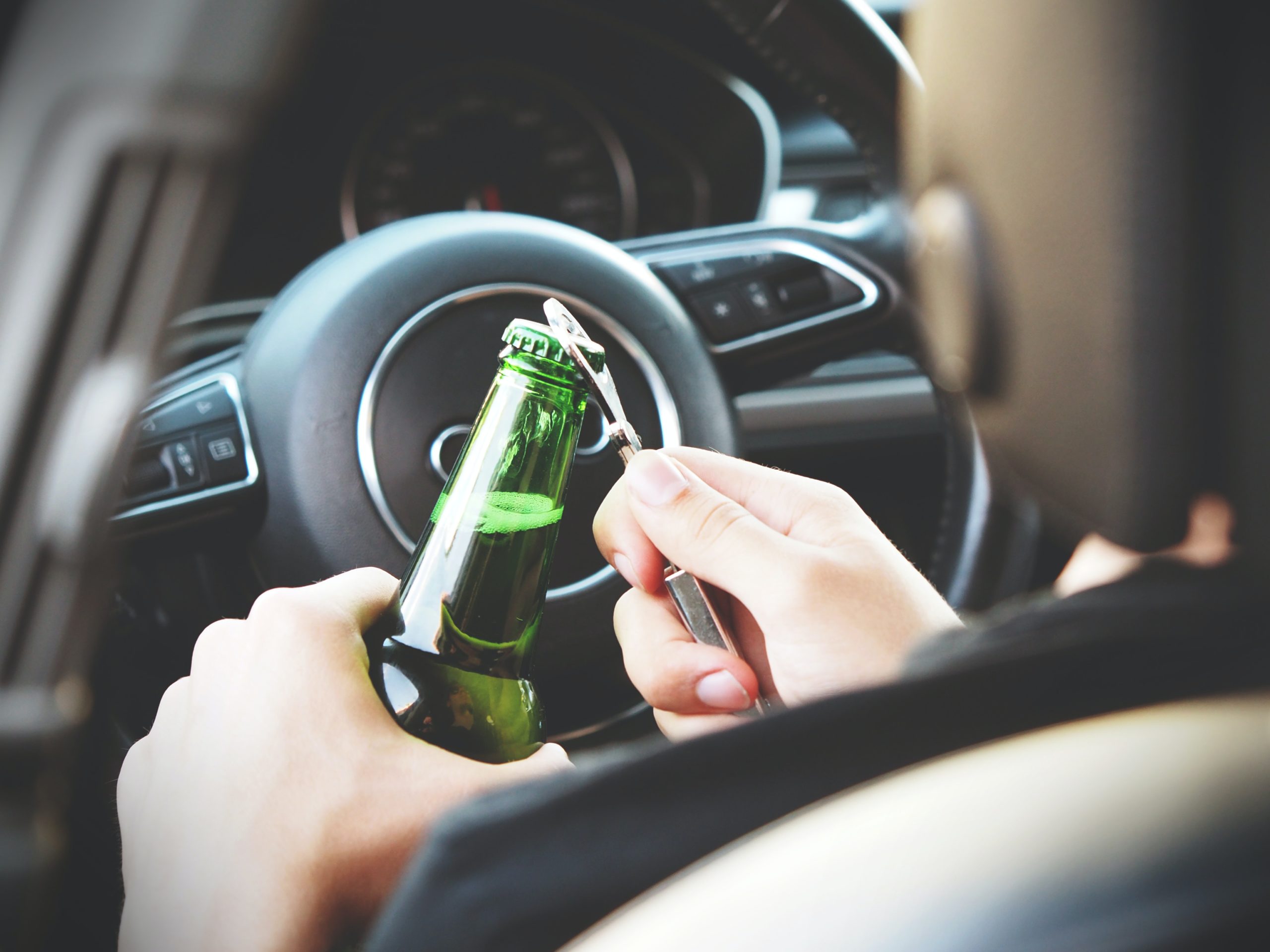 A person sitting in their car is opening a bottle of beer.