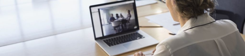 An example of a video conference showing a woman at a table with an open laptop. On the laptop screen are several people around a table.