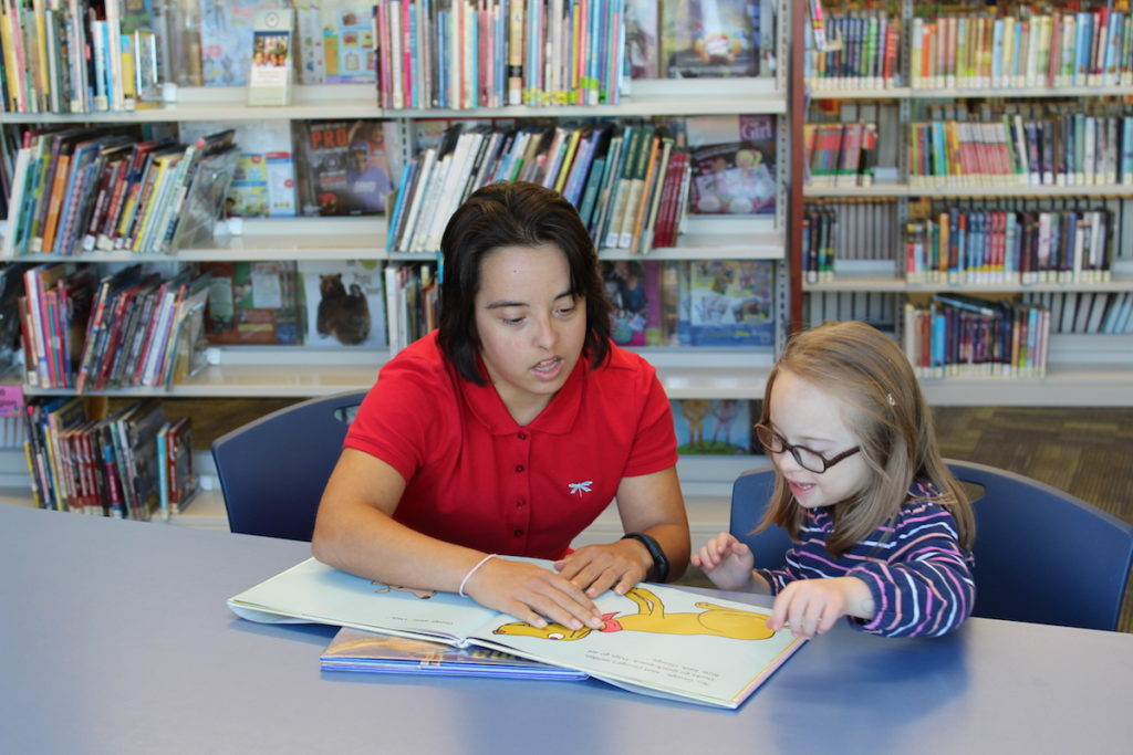 Woman with Down syndrome helping a child with Down syndrome to read.