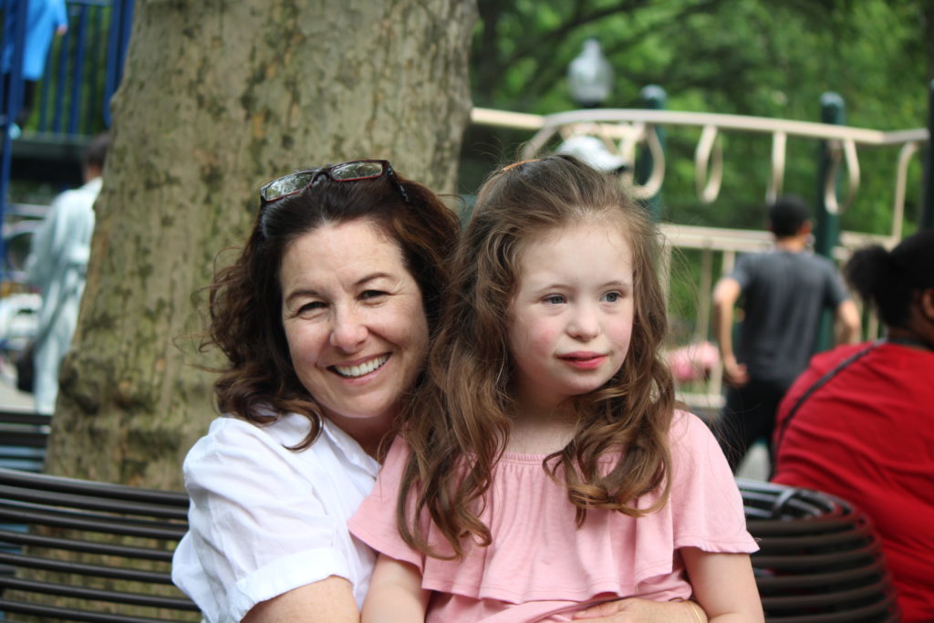 You girl with Down syndrome with long brown hair and her mother. smiling.