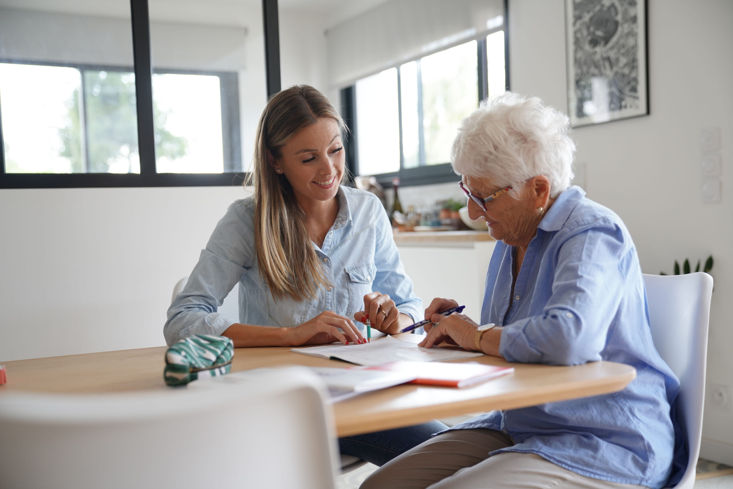 A younger woman and an older woman sitting together at a table discussing papers in front of them. The older lady is holding a pen