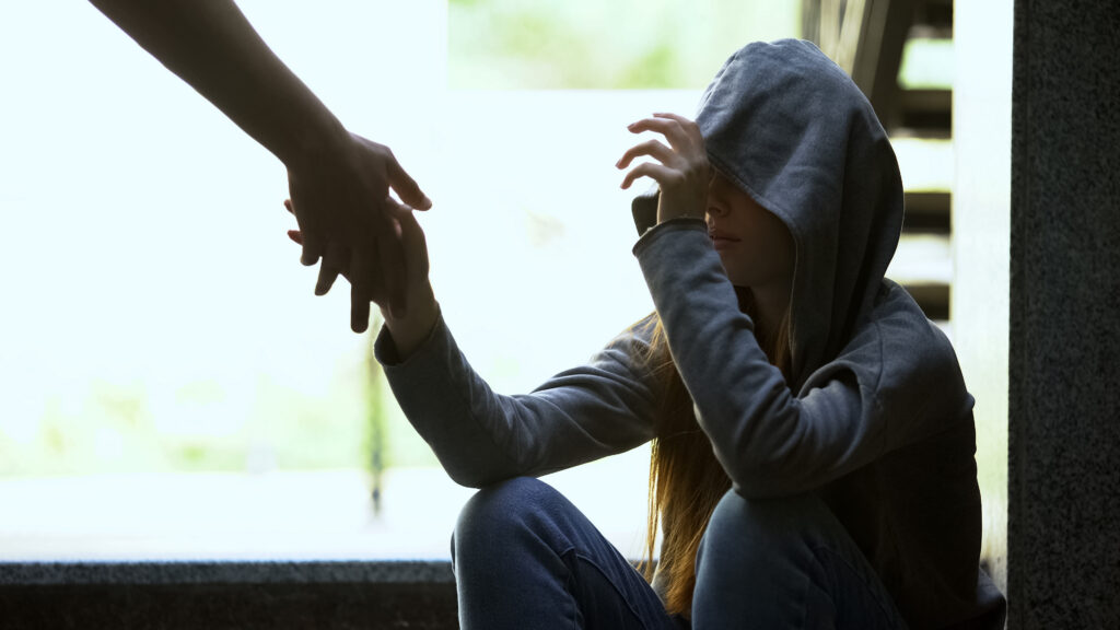 Person stretching helping hand to lonely depressed girl