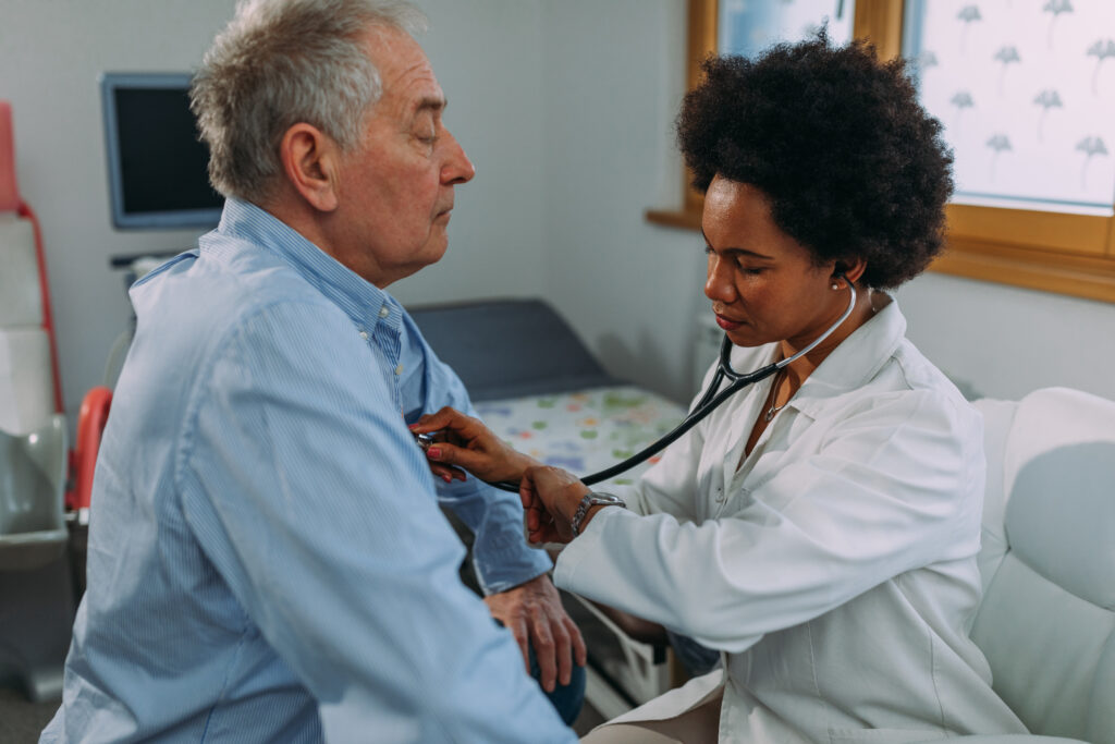 African American female healthcare working checking vitals of an older man sitting down.