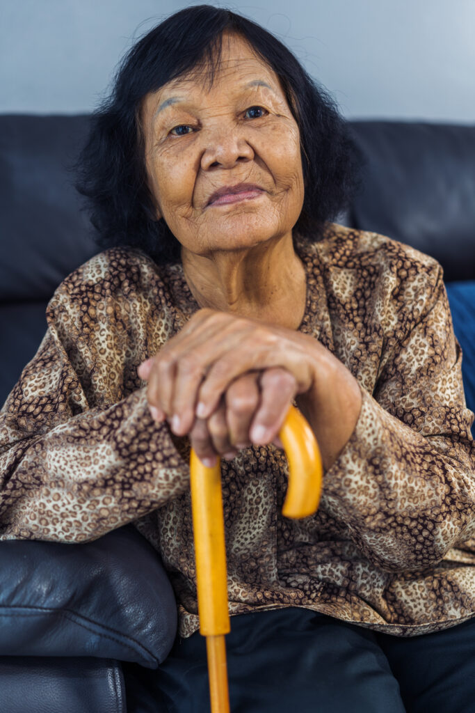 Older woman sitting on a couch holding a cane. 