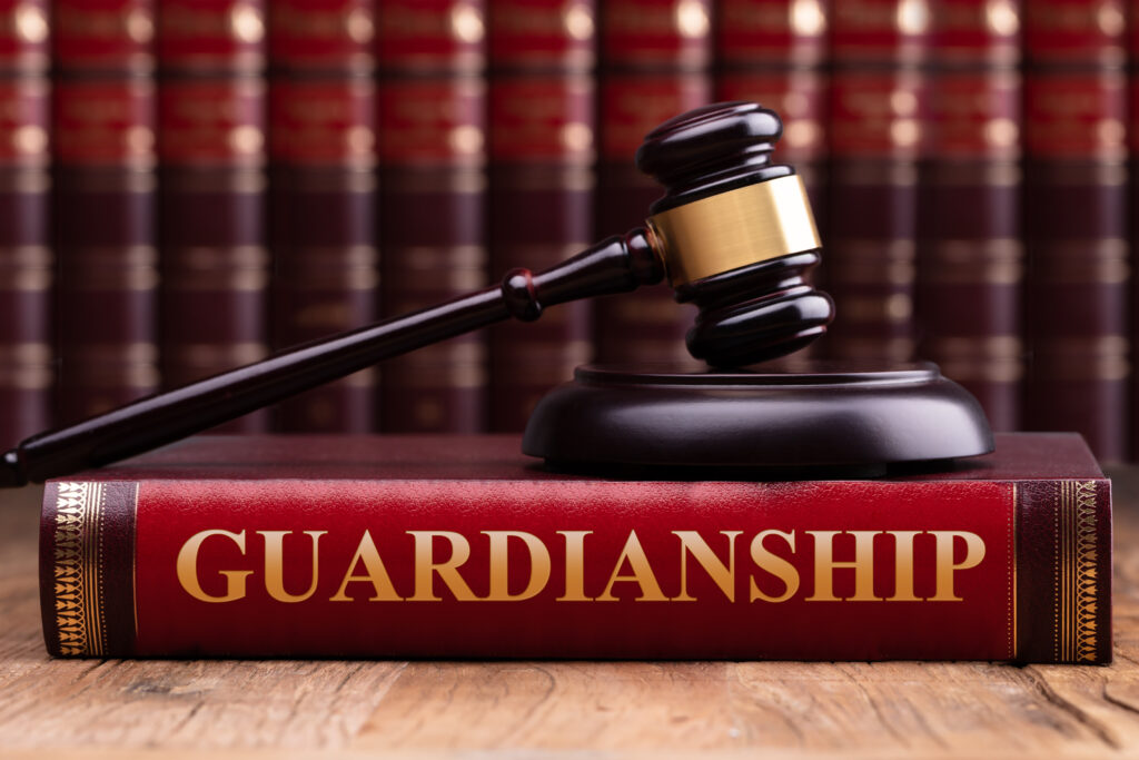 Judge gavel sitting on top of a book entitled "Guardianship" in front of a background of books. 