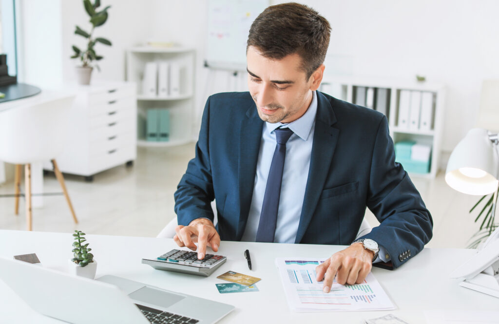 Man wearing a business suit sitting at a table with a calculator and papers