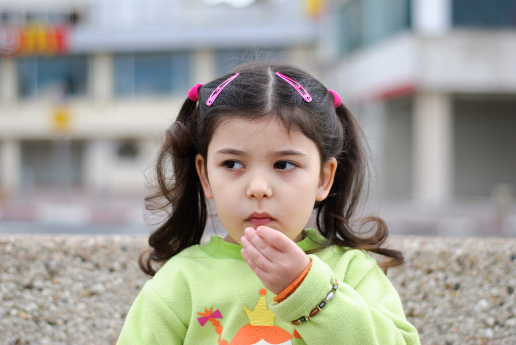 Young girl with pigtails staring off to the side and is putting hand on mouth.