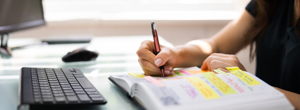 A person sitting at a computer desk writing in a planner