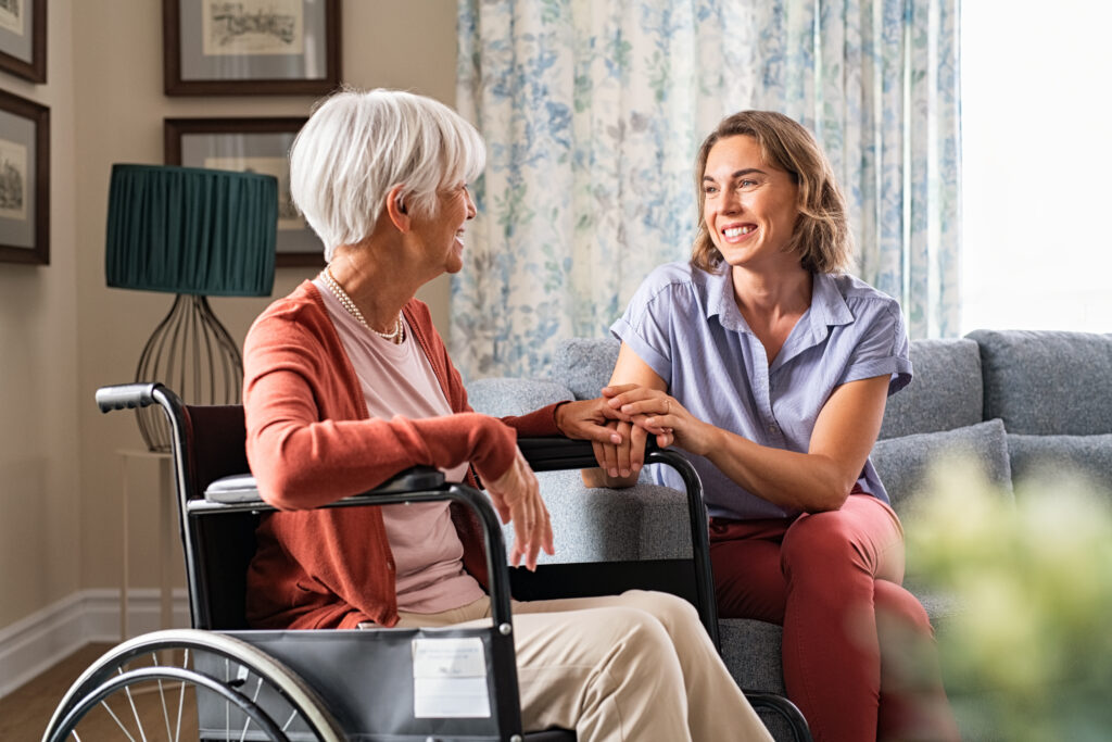 Young woman sitting on a couch talking to an elderly woman in a wheelchair