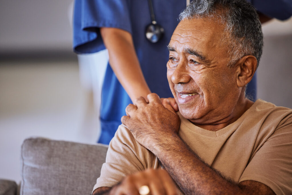 Person standing behing a man sitting on a couch with hand on shoulder.