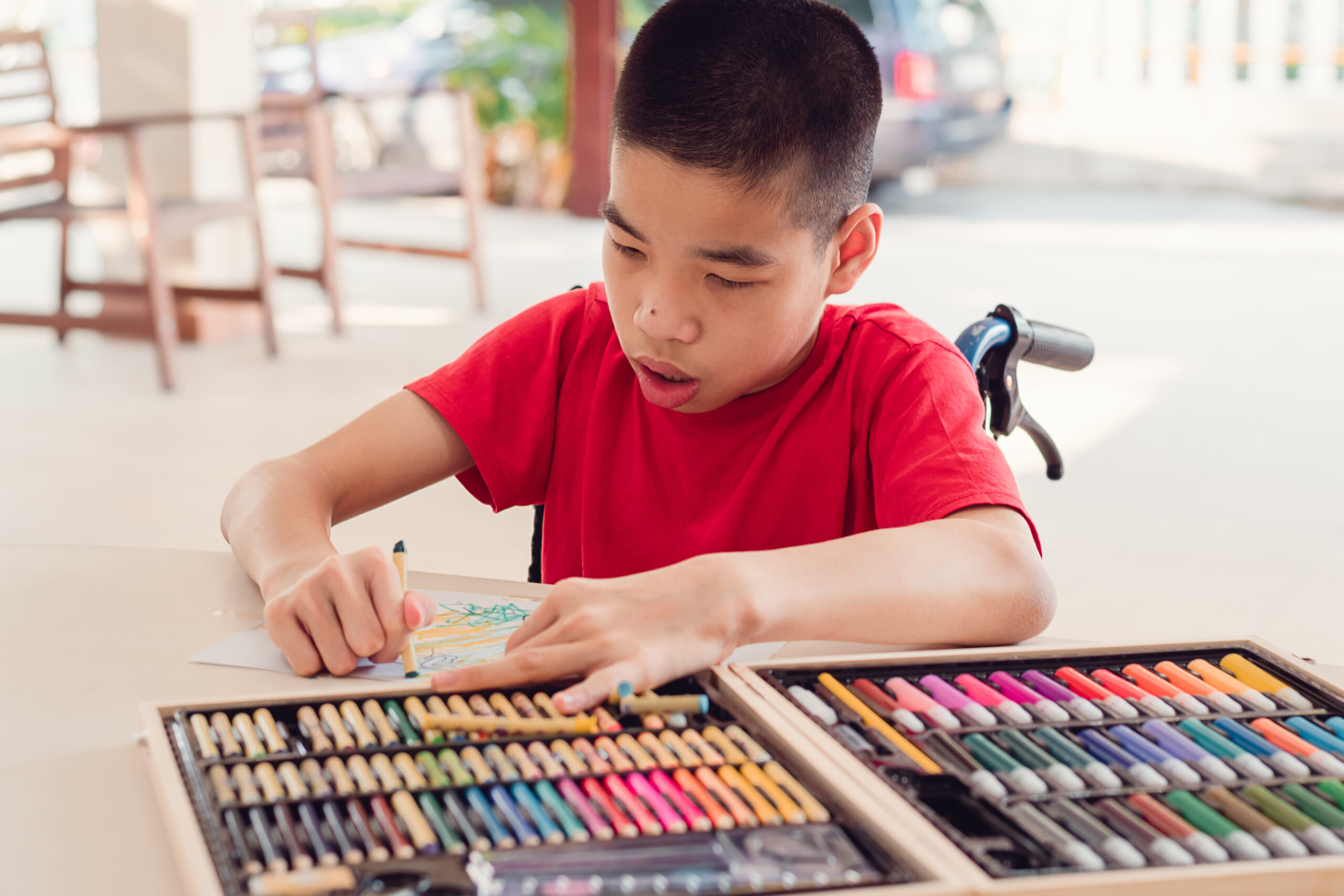 School age child in a wheelchair coloring with crayons.