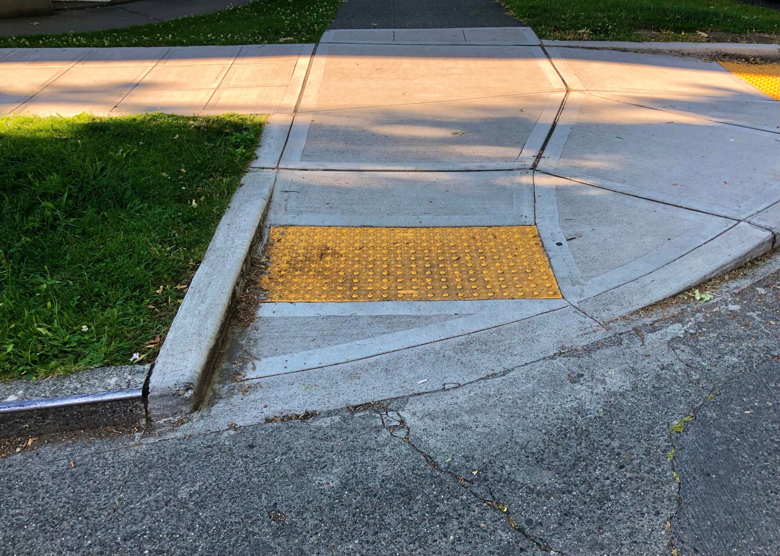 A curb cut with a yellow textured section in the sidewalk provid